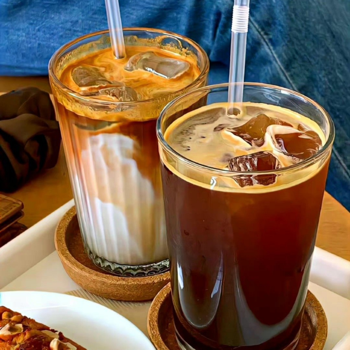 Two glasses of iced coffee with cream on wooden coasters