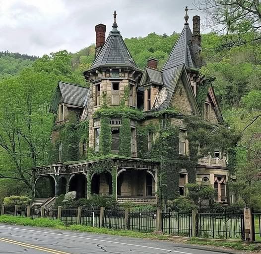 Victorian-style stone house with turrets, porch, and trees beside a road