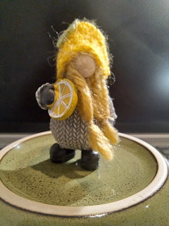 Small handmade gnome figurine with yellow hat and braids holding a lemon slice on a green plate