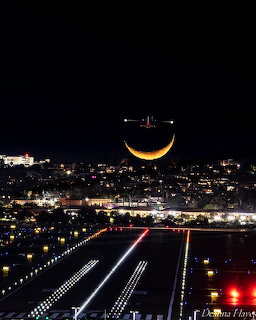 Airplane silhoueted against a crescent moon above an illuminated airport runway at night