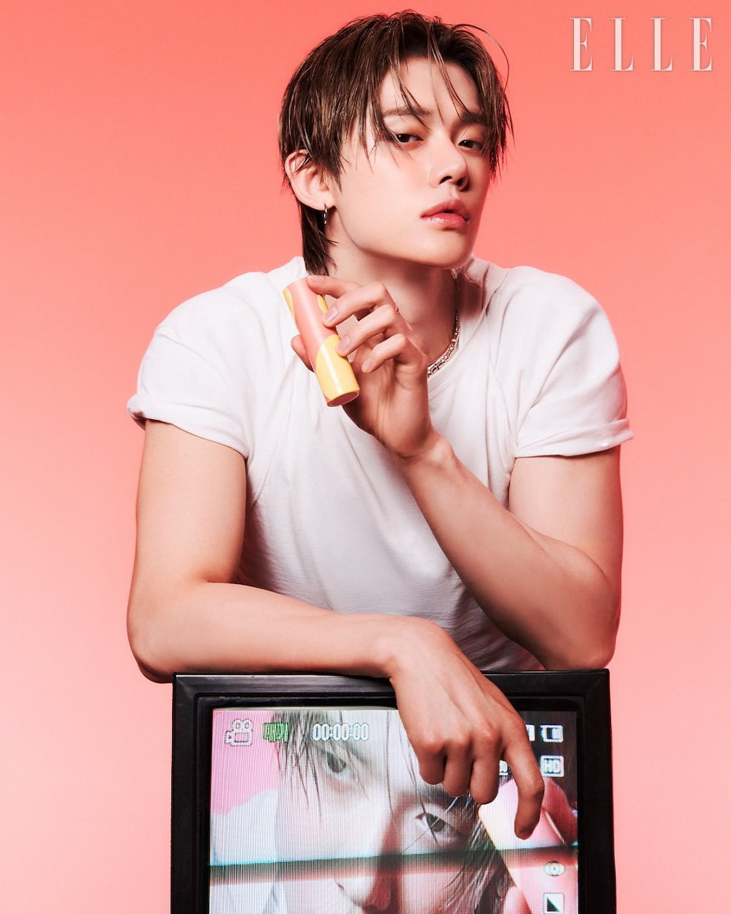 Young male K-pop idol in white t-shirt posing for ELLE magazine on pink background