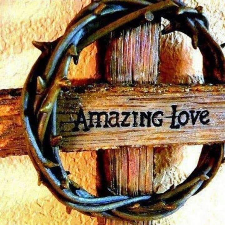 Rustic wooden sign reading 'Amazing Love' encircled by a dark woven wreath on weathered wood