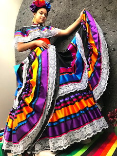 Woman dancing in vibrant Mexican Folklorico dress with purple, orange, and yellow stripes and white lace
