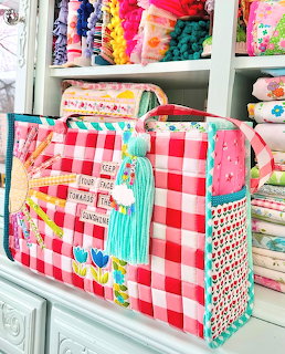 Pink gingham handbag with flowers and tassel on shelf with colorful fabrics