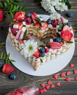 Heart-shaped cake topped with strawberries, blueberries, macarons, and pink roses on wooden table