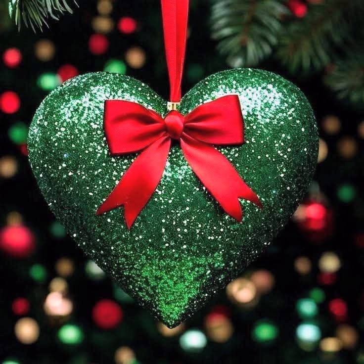 Sparkling green heart ornament with red bow on Christmas tree