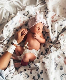 Newborn baby resting on floral blanket with mother's hand touching face