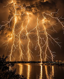 Multiple lightning bolts striking over a body of water at night with reflections on the surface