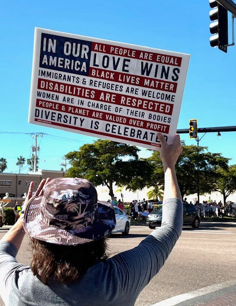 Person holding a protest sign at a street intersection under a blue sky