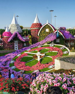 Large floral clock display with flower-covered castlelike structures at a botanical garden
