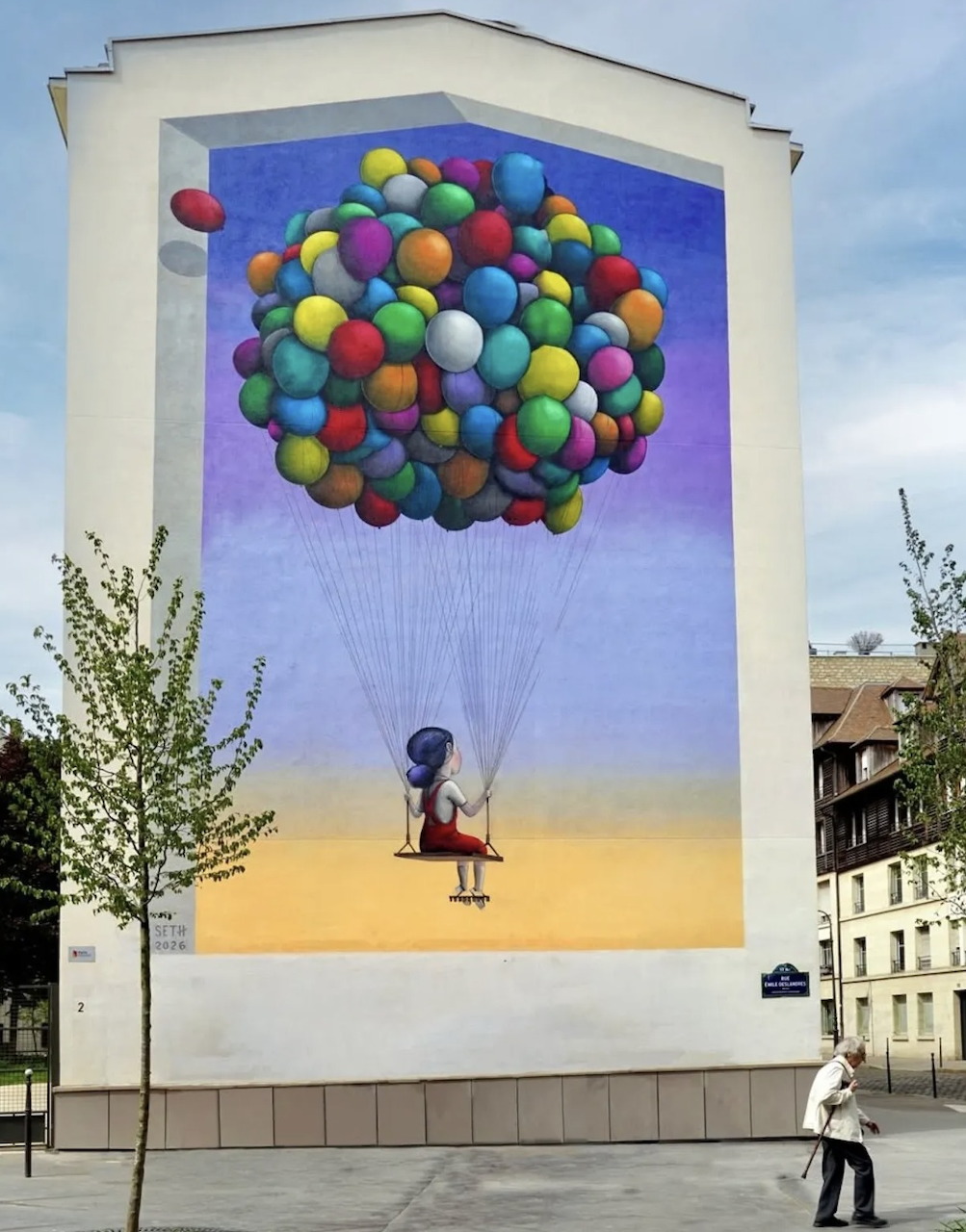 Street art mural of a girl holding many colorful balloons on the side of a building in Paris