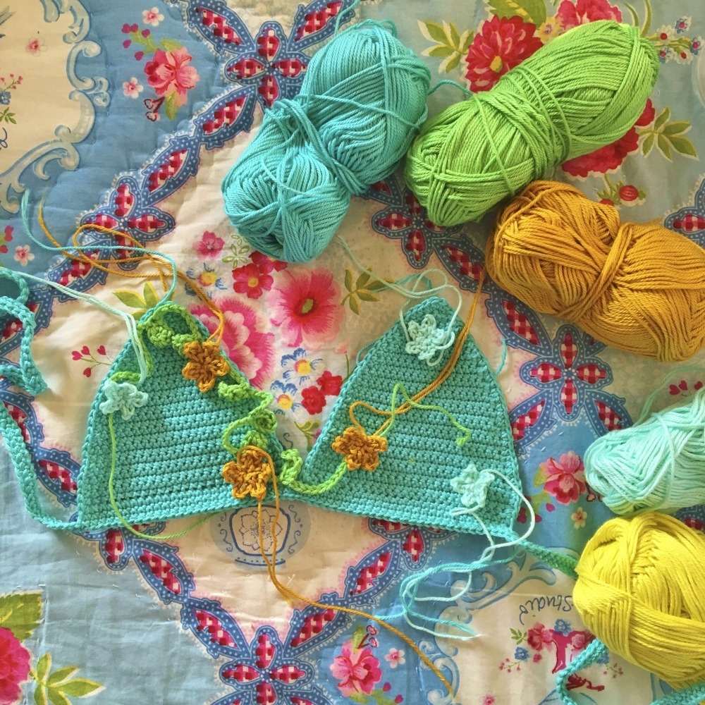Turquoise crocheted bikini top on floral fabric with colorful balls of yarn