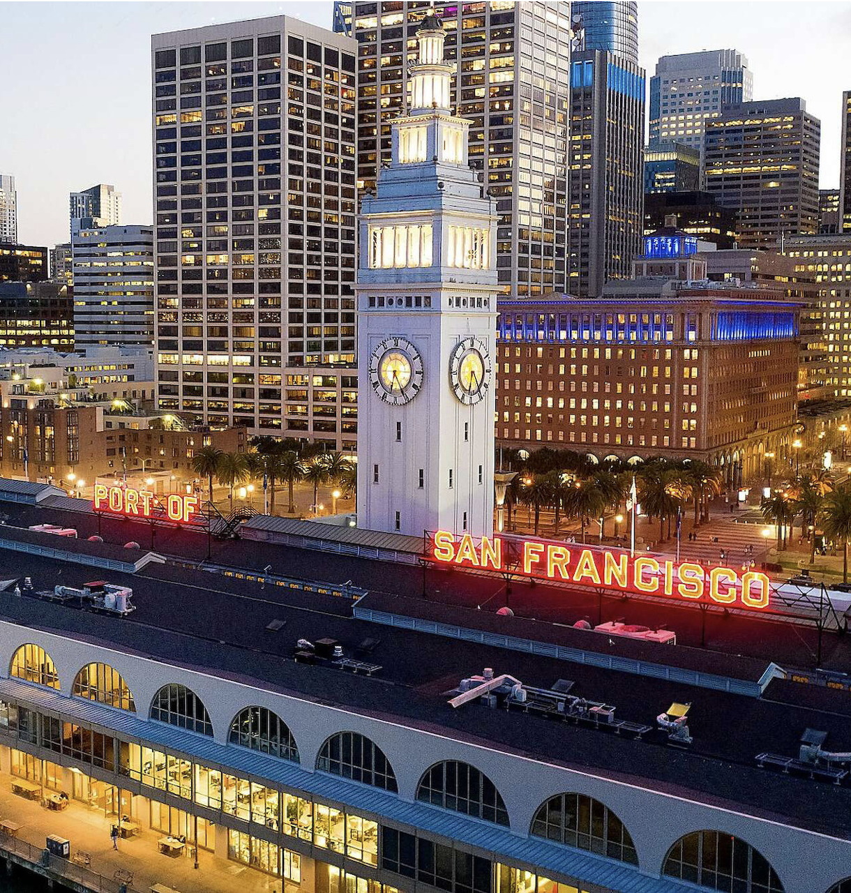 San Francisco Ferry Building clock tower illuminated at dusk with city skyline in background