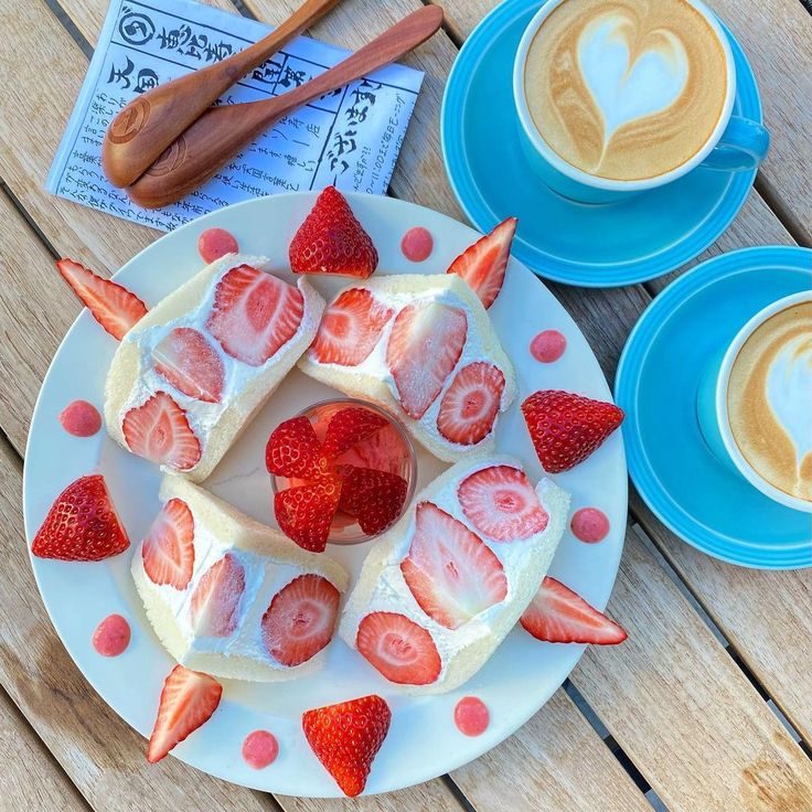 Overhead view of strawberry fruit sandwiches on a plate with two cups of latte art