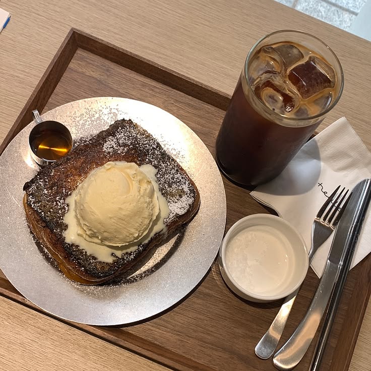 French toast with ice cream and powdered sugar, iced coffee, and syrup on a wooden tray