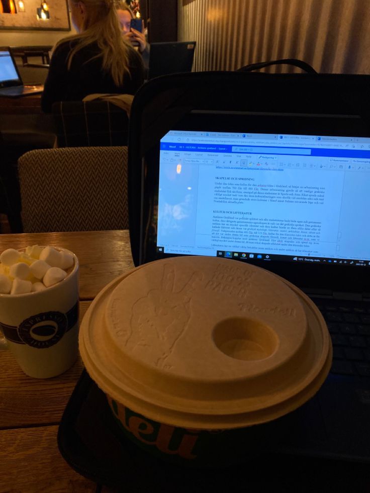 Laptop open on a café table with a takeaway coffee cup and a marshmallow drink in a cozy interior