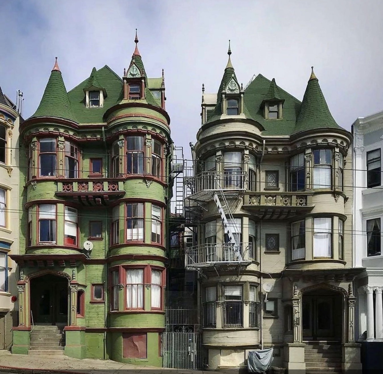 Two ornate Victorian houses with green roofs, bay windows, and exterior staircases