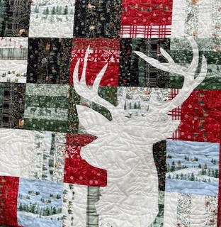 Patchwork quilt with white deer and antler silhouette on red, green, and black Christmas fabric squares