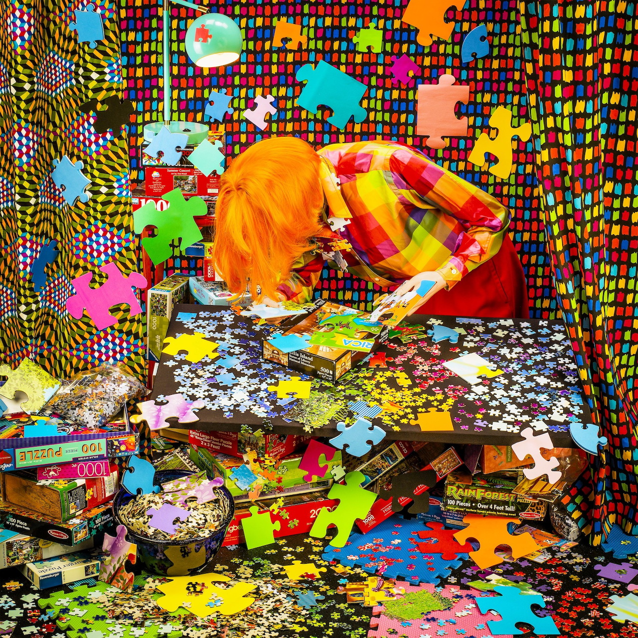 Woman with orange hair sorting puzzle pieces in a brightly patterned room