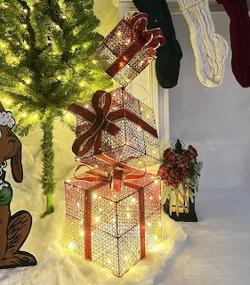 Three glowing white gift boxes with red bows stacked beside lit Christmas tree