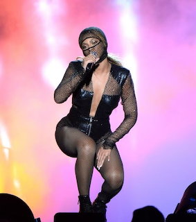 Female singer performing on stage in mesh outfit with colorful stage lighting behind her