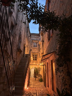 Narrow cobblestone alley with a staircase and warmly lit old buildings at dusk
