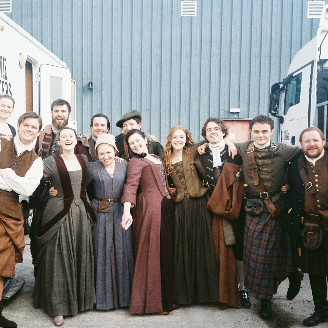 Group of people in period costumes posing outdoors between trailers