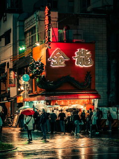Rainy night street in Japan with illuminated red restaurant sign and people walking with umbrellas