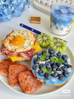 Breakfast plate with croissant, egg sandwich, kiwi, blueberries, and blue flowers beside a decorated mug