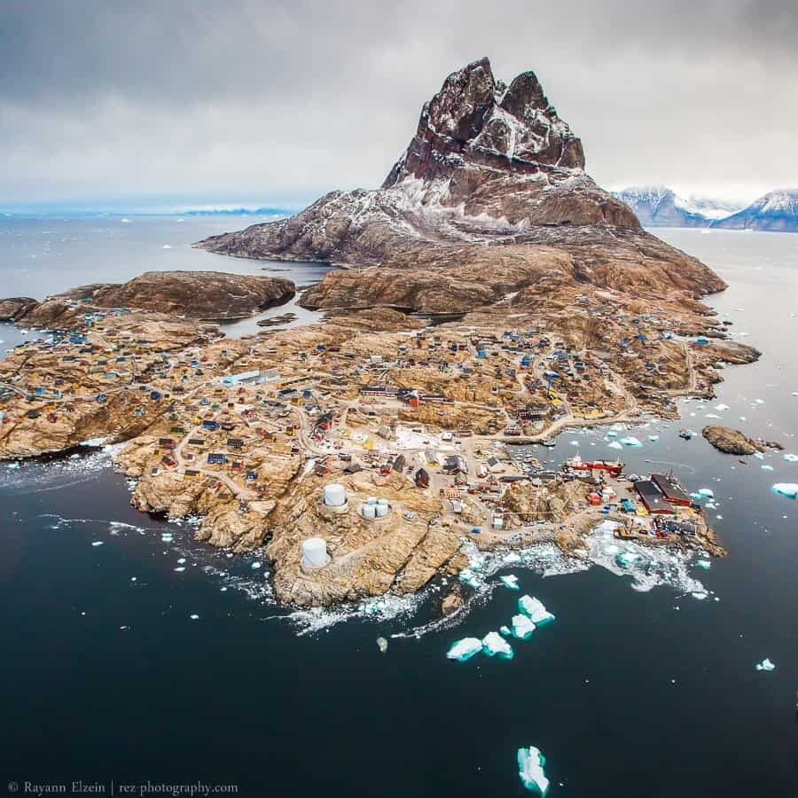 Rocky Arctic coast with colorful houses below a snow-dusted mountain by dark water