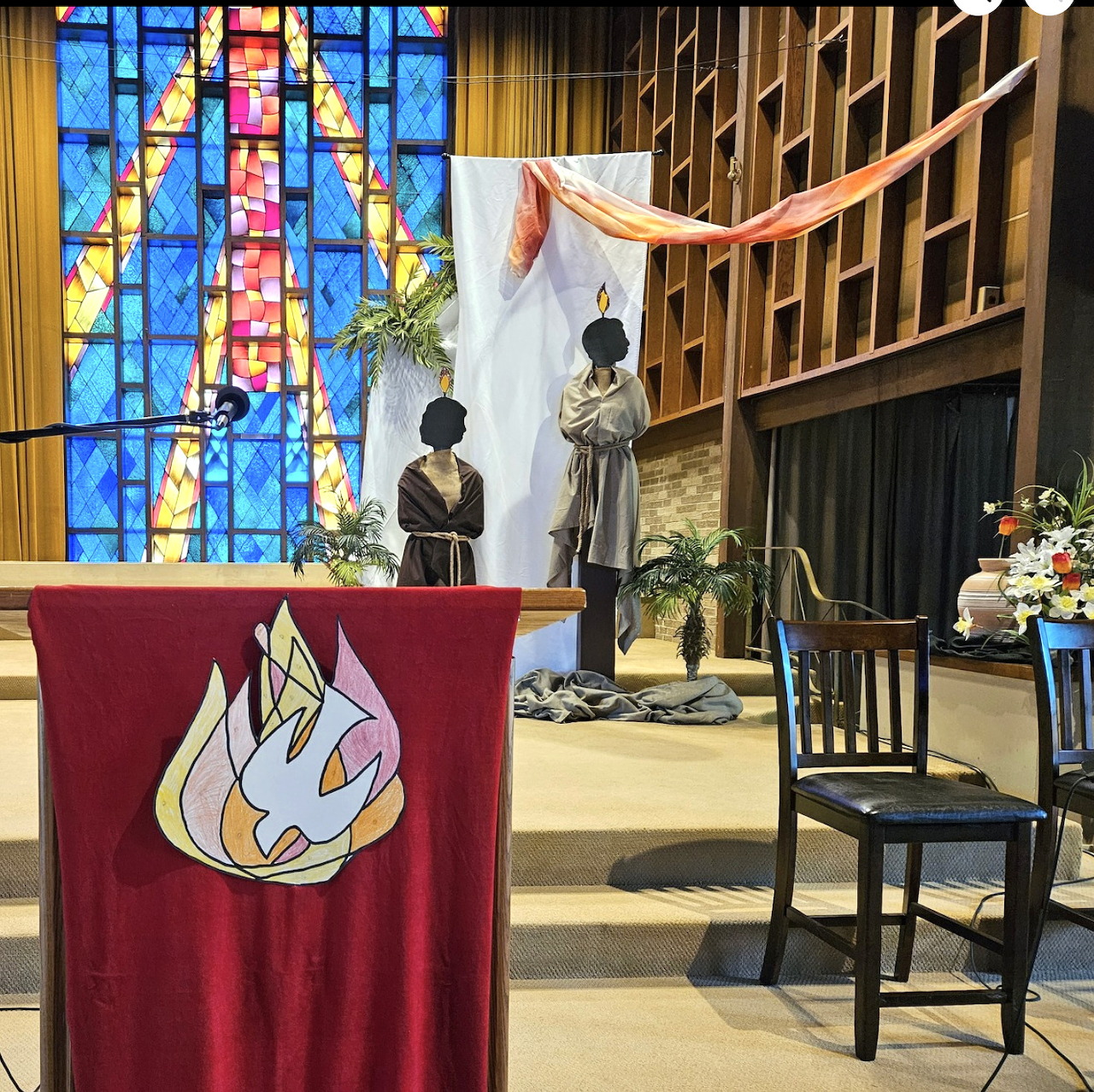 Church altar with Pentecost banner, stained glass window, and people during service