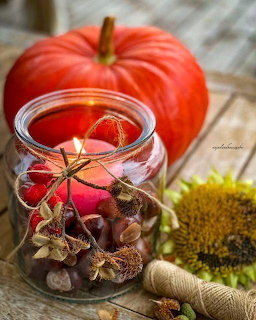 Glass candle jar with autumn decorations, orange pumpkin, dried flowers and twine on wooden table