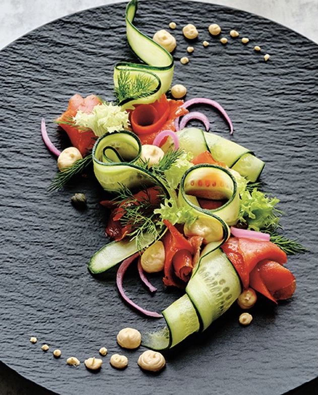 Artfully arranged fresh vegetable salad on a dark slate plate with cucumber ribbons and tomatoes