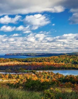 Aerial view of lake surrounded by autumn trees with colorful fall foliage under cloudy blue sky