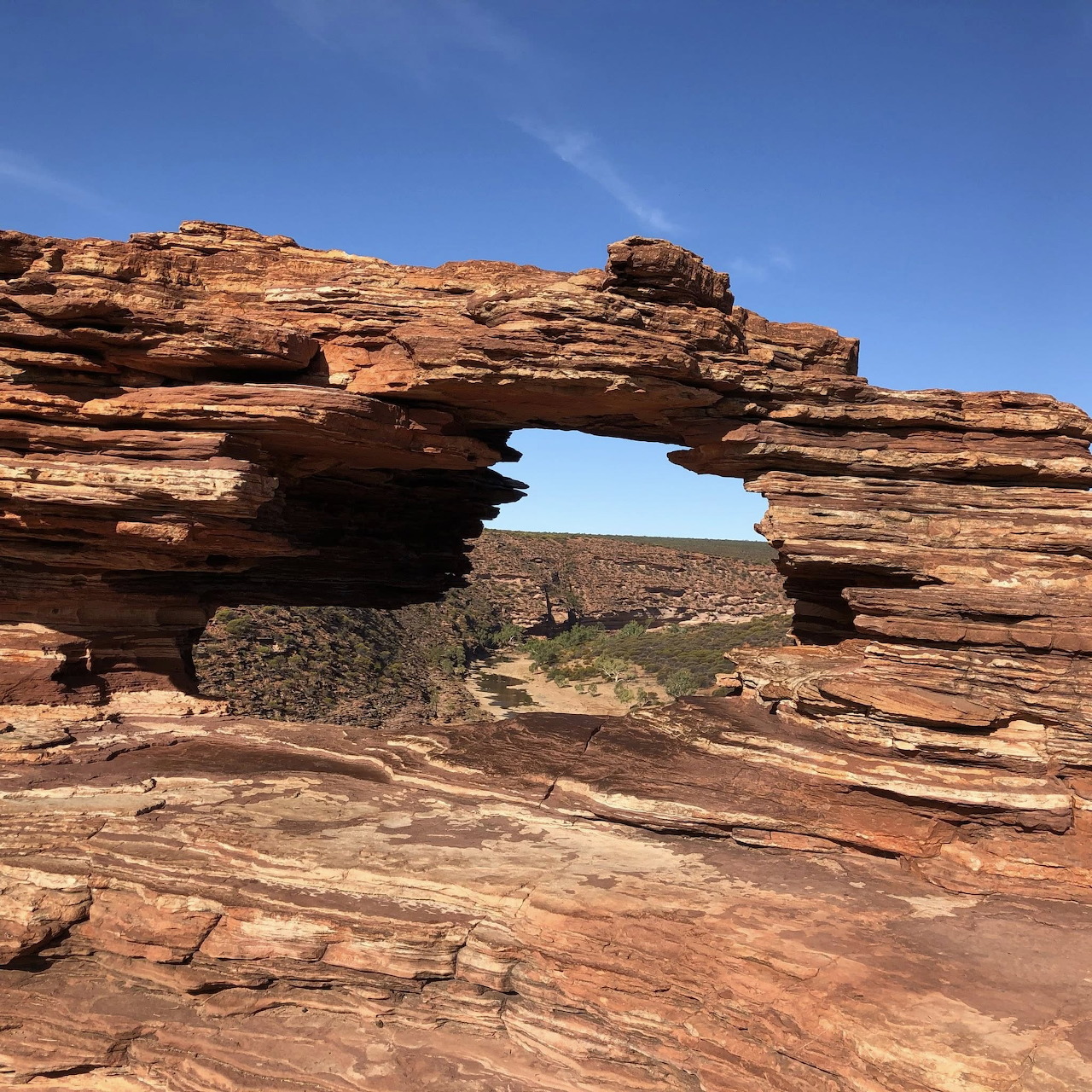 Natural red sandstone arch with horizontal layered striations in Kalbarri against clear blue sky