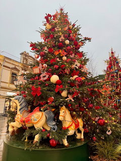 Decorated Christmas tree with red and gold ornaments and carousel horse figures at its base outdoors
