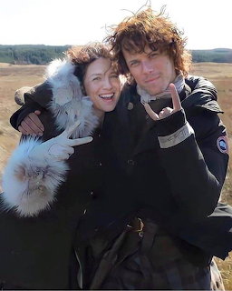 Man and woman in historical costumes posing together on a moorland making hand gestures