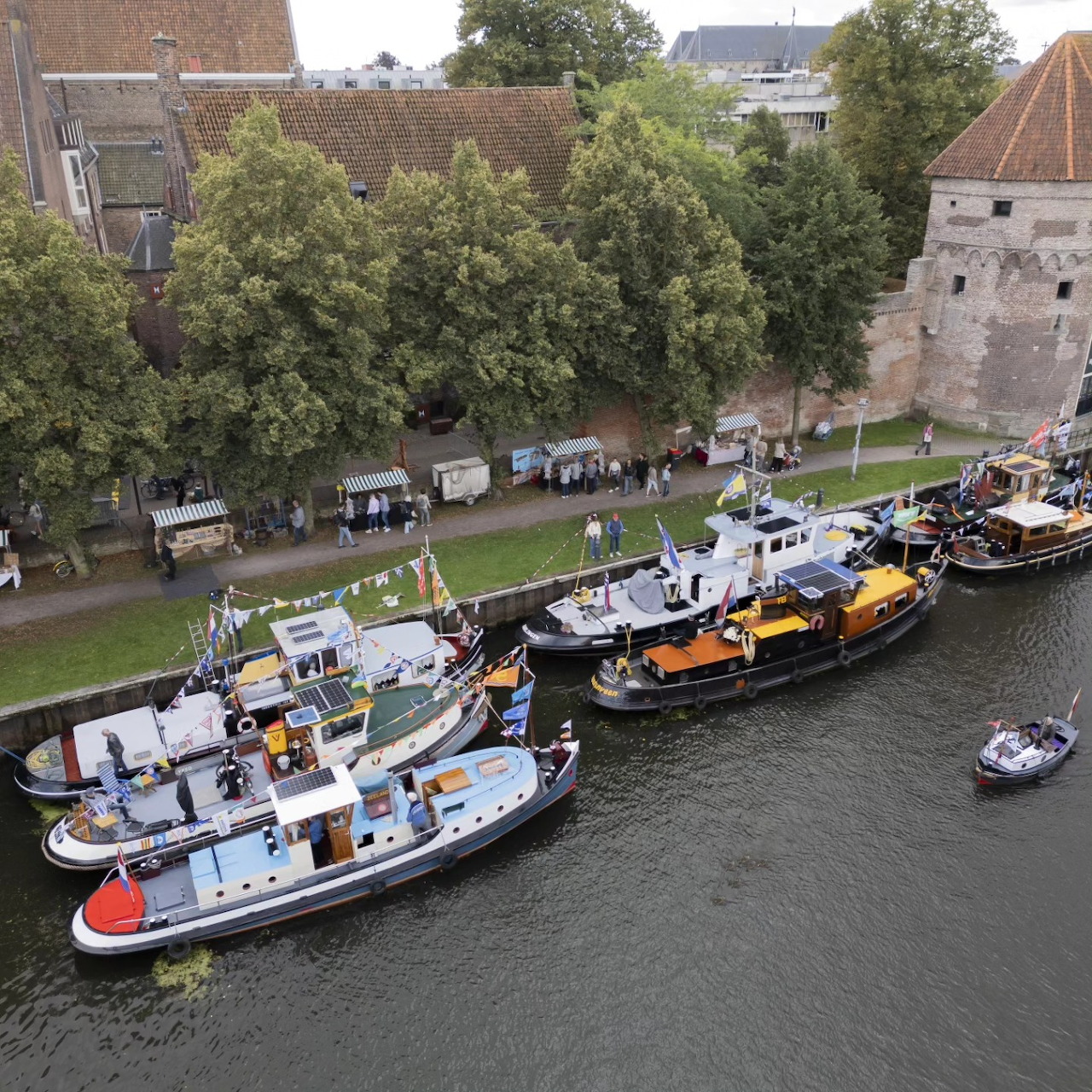 Boats moored along a canal beside trees, historic buildings, and a stone tower in Zwolle