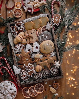 Wooden tray of assorted Christmas cookies with gingerbread, candy canes, pine branches, and warm bokeh lights