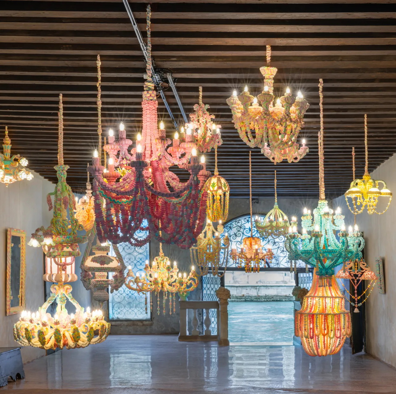 Multiple decorative glass chandeliers in pink, amber, blue and turquoise hanging at different heights in modern gallery