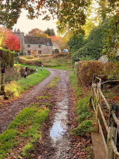 Mudy country lane leading to a stone cottage surrounded by autumn trees with colorful foliage