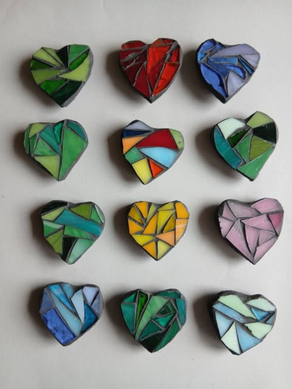 Twelve colorful heart-shaped stained glass pieces arranged in rows on white background