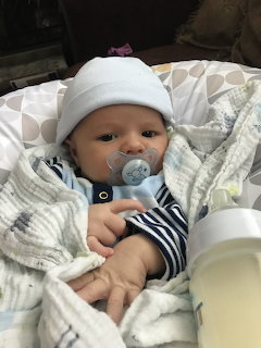 Baby in white hat and striped clothing with pacifier resting on white blanket