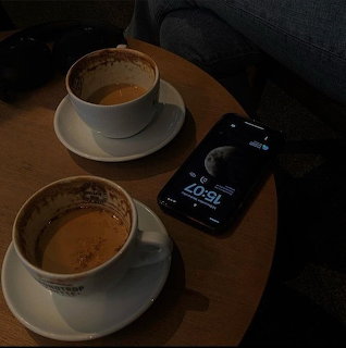 Two cups of coffee on saucers next to a smartphone on a small wooden table