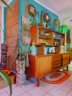 Mid-century modern teak sideboard with tiki decor, plants, and colorful accessories in a retro living room