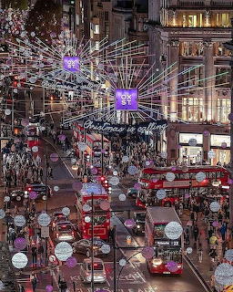 Oxford Street London at Christmas with glowing overhead lights, red buses, and crowds of shoppers at night