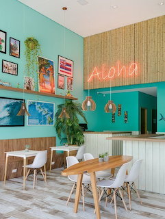 Tropical restaurant interior with turquoise walls, neon Aloha sign, pendant lamps, and wooden dining tables