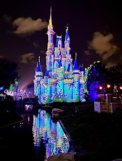 Illuminated Cinderella Castle with colorful lights reflecting in water at night