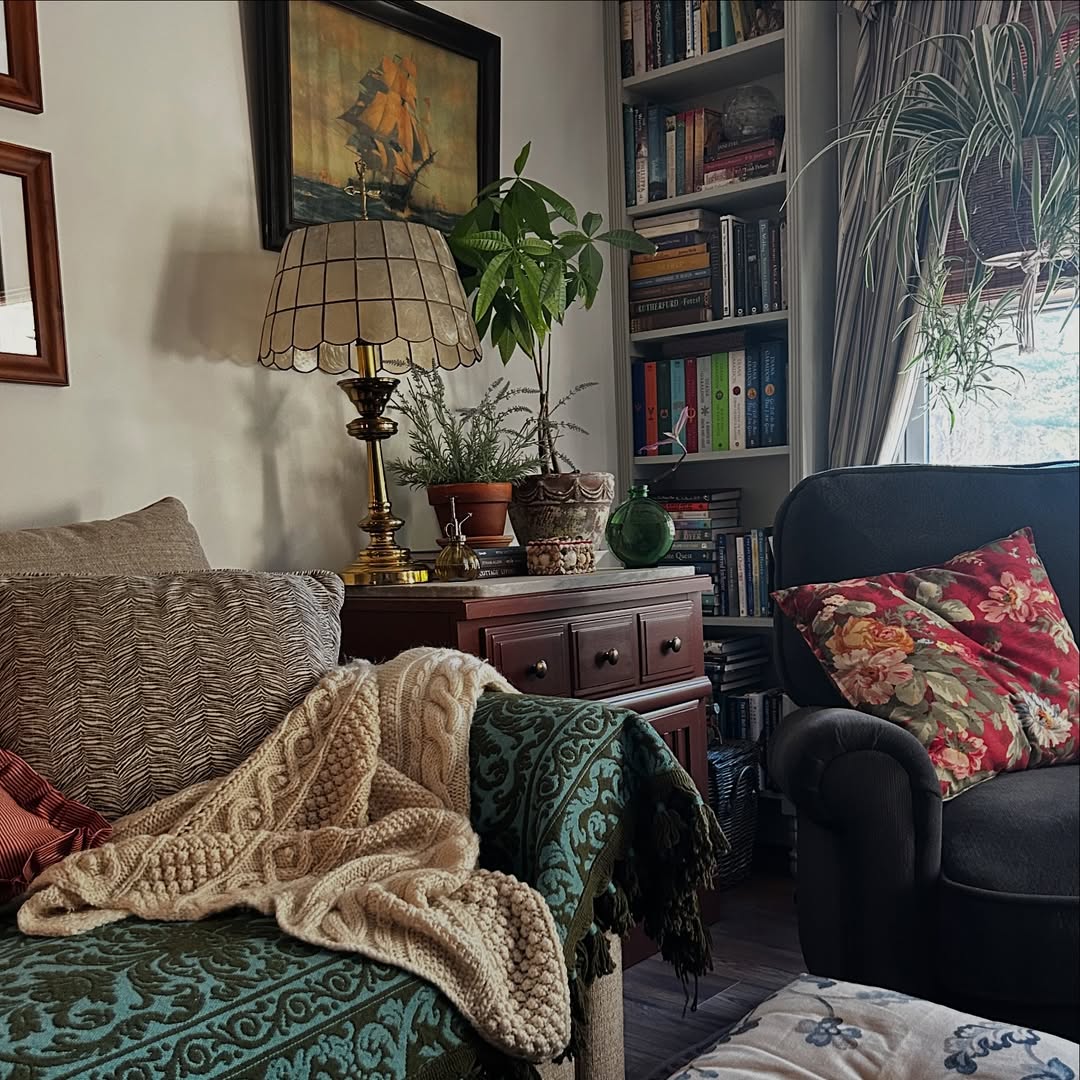 Cozy living room with armchair, knit blanket, bookshelf, plants, and vintage trunk