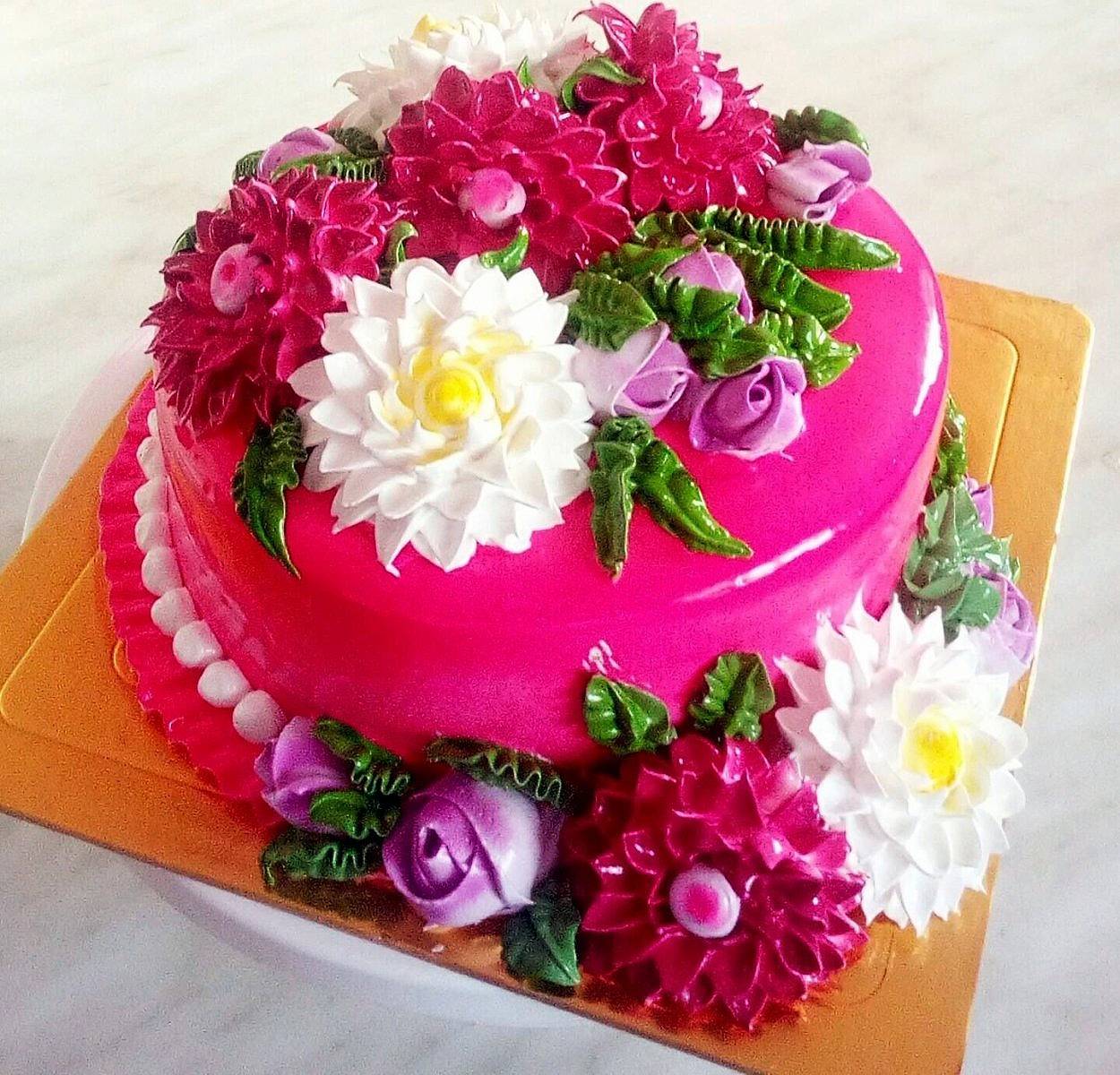 Round pink cake with white, magenta, and purple sugar flowers on orange board